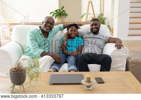 Portrait of senior african american fon couch smiling with adult son and grandson embracing. happy three generation family spending time together at home.