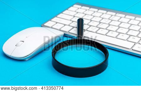 Magnifying Glass With Computer Keyboard And Mouse On Blue.