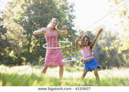 Woman And Young Girl Outdoors Using Hula Hoops And Smiling