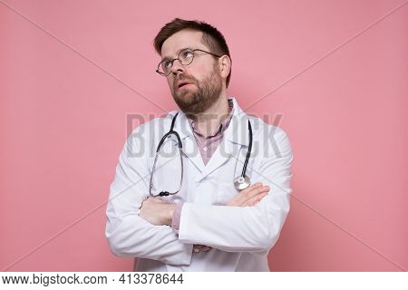 Tired Male Doctor In A White Coat, With A Stethoscope Around Neck, Crossed Arms And Looked Up Apathe