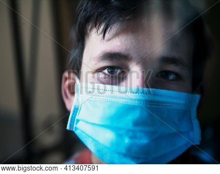 Boy With A Medical Mask Looks Sadly Out Of The Window During His Confinement Because Of Convid 19
