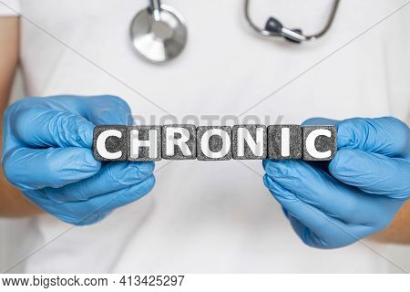 Chronic - Word From Stone Blocks With Letters Holding By A Doctor's Hands In Medical Protective Glov