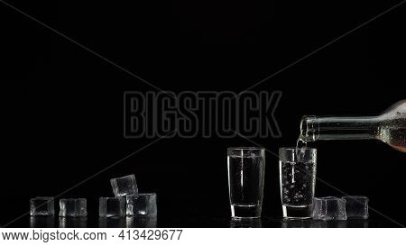 Two Hands With Glasses Of Vodka Making Cheers On Black Background With Ice Cubes. Celebration Of Bus