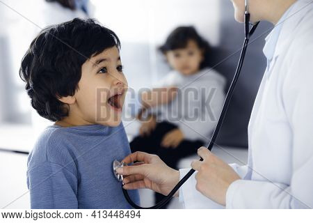 Doctor-woman Examining A Child Patient By Stethoscope. Cute Arab Boy And His Brother At Physician Ap