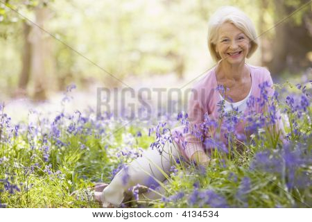 Kvinden sidder udendørs med blomster smilende