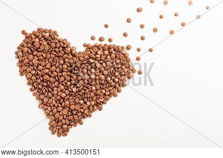 Chocolate Callets In Bulk On A White Background In The Form Of A Heart. The Concept Of Tempered Choc