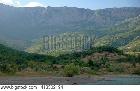 The Shore Of A Mountain Lake In The Midst Of Inaccessible Rocks, Surrounded By A Green Forest.