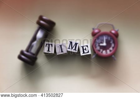 In Selective Focus Of Time Word Written On Wood Block Put At The Middle Of Blurred Sandclock And Red