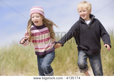 Twee jonge kinderen lopen op strand hand in hand glimlachen