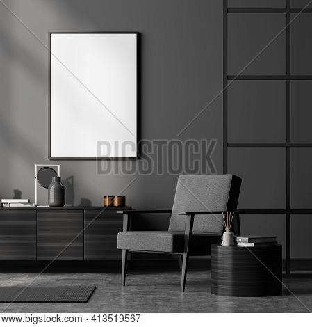 Dark Living Room Interior With Grey Armchair, Wooden Drawer And Coffee Table With Books And Decorati