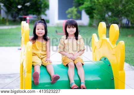 The Sisters And The Younger Sisters Sit On Children's Tunnel Player In Playground. Child Smiled Swee