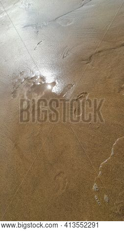 Footprints Of Human Feet On The Sand Near The Water On The Sea Beach.