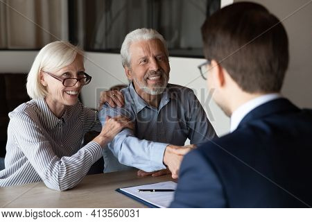 Smiling Older Couple Clients Handshake Relator At Meeting