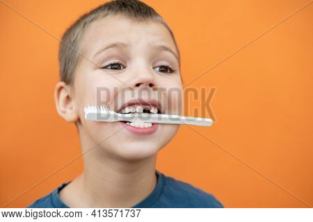 Boy Without Milk Upper Tooth In Blue T-shirt Holds Toothbrush In His Mouth On The Orange Background.