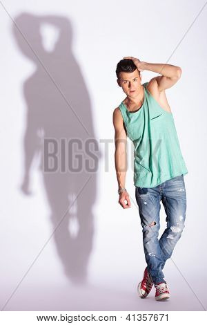 voller Länge Bild von einer jungen legerer Mann posiert mit seiner Hand durch sein Haar, auf grau, mit hart 