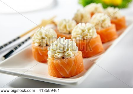 Philadelphia Sushi Roll made with Smoked Salmon. Maki sushi topped with cream cheese. White plate with wooden chopstick on white table