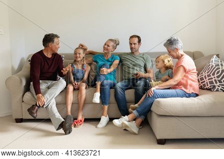 Senior caucasian man sitting on couch talking with his smiling three generation family. happy three generation family spending time together at home.