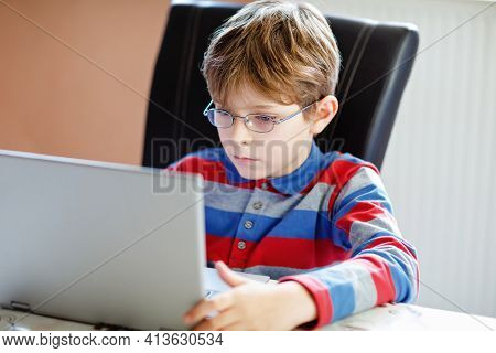 Happy Healthy Kid Boy With Glasses Making School Homework At Home With Notebook. Interested Child Wr