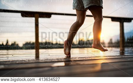 Unrecognizable Small Daughter Playing In Rain On Patio Of Wooden Cabin, Holiday In Nature Concept.