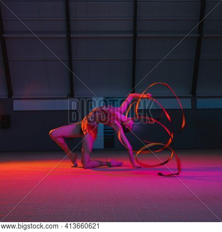 Graceful Caucasian Girl Gymnast Isolated Over Colored Background In Neon Light