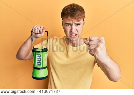 Young caucasian man holding big electric lantern annoyed and frustrated shouting with anger, yelling crazy with anger and hand raised 