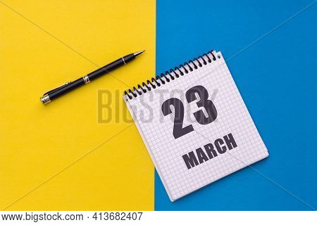 March 23th. Day 23 Of Month, Calendar Date. A Notebook With A Spiral And A Pen Lies On A Yellow-blue