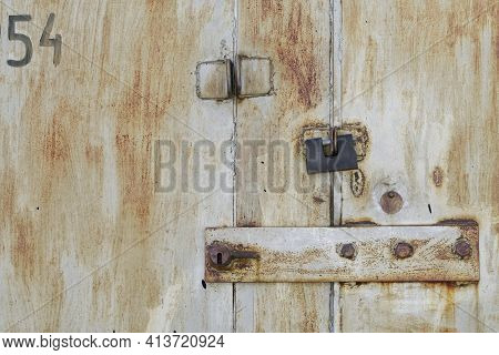 A Rectangular Padlock Hangs From The Old Rusty Metal Doors Of An Abandoned Garage Or Warehouse Next 