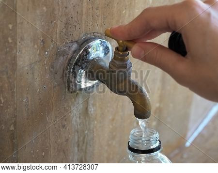 The Hand Turns The Valve Of The Tap With Water Flowing Into A Plastic Bottle
