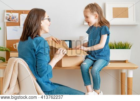 Mother and daughter are unpacking cardboard box at home.