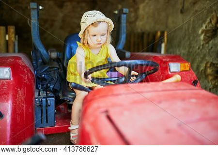 Adorable Toddler Girl Playing On Old Red Tractor On Gally Farm Near Paris, France. Outdoor Summer Ac