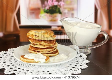 หวาน pancakes บนแผ่น ด้วยครีมเปรี้ยวบนโต๊ะในห้อง