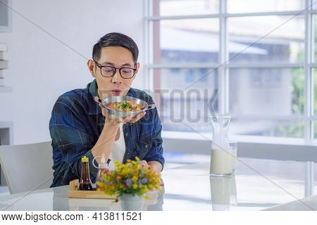 Young Man Wearing Glasses Sitting Looking At The Fried Egg Served On A Pan With Colorful Toppings Se