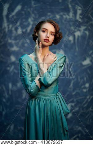 Attractive sophisticated girl in an elegant dress stands grunge background. Art fashion. Hair and makeup in the style of the 20s. 