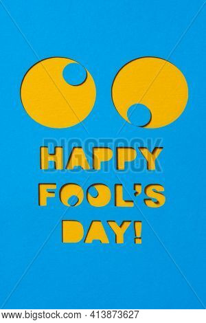 a pair of funny eyes and the text happy fools day cut out in a blue paperboard, against an orange background