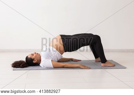 Young Flexible Pregnant Woman Doing Gymnastics On Rug On The Floor On White Background. The Concept 