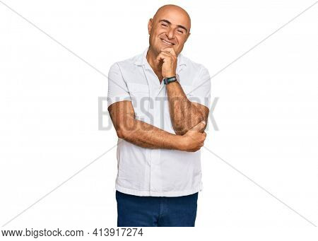 Mature middle east man with mustache wearing casual white shirt with hand on chin thinking about question, pensive expression. smiling and thoughtful face. doubt concept. 