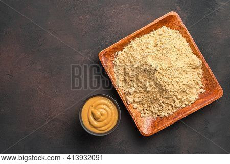 Dry Mustard Powder In A Wooden Plate And Ready-made Pasty Mustard On A Brown Background. Minimalisti