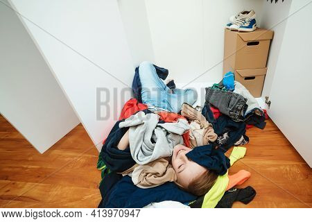 Lazy Boy Lying On The Thrown Clothes On The Floor. Mess In Open Wardrobe. Untidy Clutter Clothing Cl