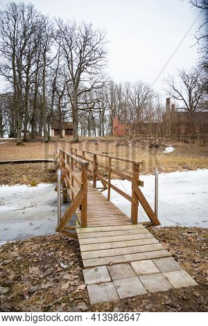Wooden Bridge Over A Frozen River In The Park With Lighting Lanterns And Wooden Protective Barriers.