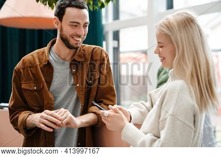 Happy young couple talking while standing insode cafe, holding mobile phone