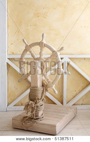 Beautiful wooden ship wheel with wire rope in light room with yellow walls.