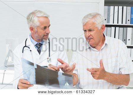 Male doctor explaining x-ray report to senior patient in the medical office