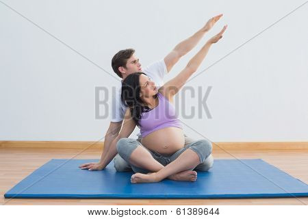 Trainer sitting with pregnant woman doing yoga in a fitness studio