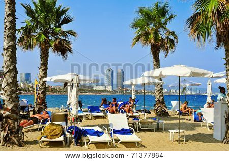 BARCELONA, SPAIN - AUGUST 19: Bathers lying in loungers in Sant Sebastia Beach on August 19, 2014 in Barcelona, Spain. In the background, Mapfre Tower and Hotel Arts, two of the landmarks in the city