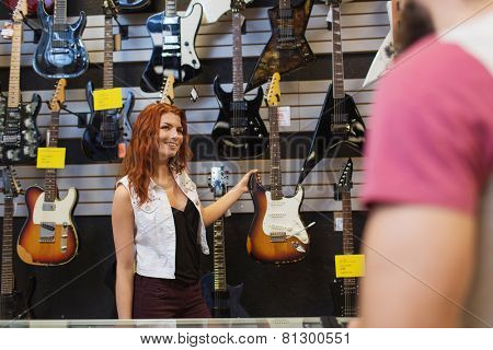 music, sale, people, musical instruments and entertainment concept - assistant showing electric guitar to customer at music store
