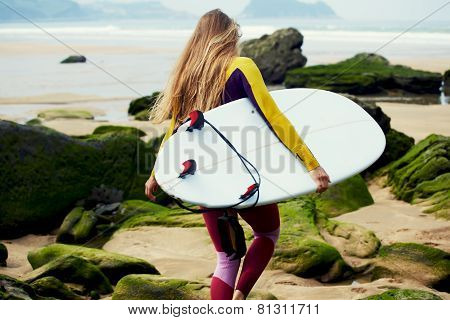 Blond long-haired girl dressed in wetsuit walking to the ocean ready to surfing