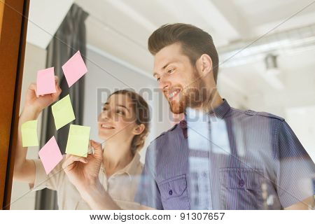 business, startup, planning, management and people concept - happy creative team writing on stickers at office glass board