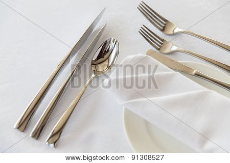 table setting, silverware and eating concept - close up of cutlery set wrapped with napkin and plate on restaurant table