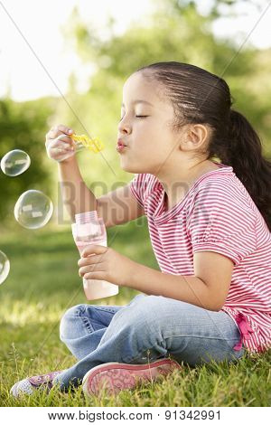 Young Hispanic Girl Blowing Bubbles In Park