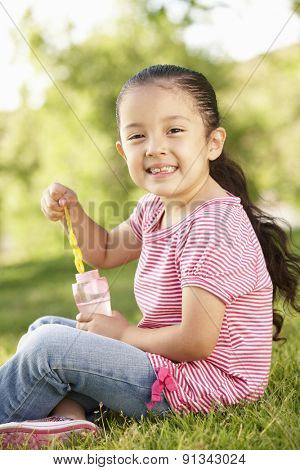 Young Hispanic Girl Blowing Bubbles In Park